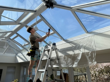 Technician installing solar control window film inside a conservatory roof, improving temperature regulation and glare reduction for residential property.