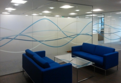 Decorative frosted window film with blue wave design applied to office glass partition, providing privacy and modern branding for commercial workspace interiors