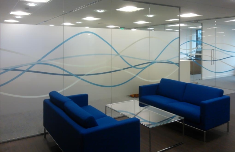 Decorative frosted window film with blue wave design applied to office glass partition, providing privacy and modern branding for commercial workspace interiors